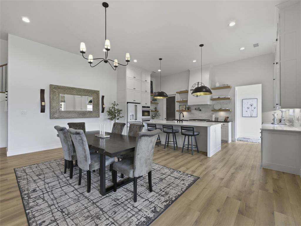 4211 Azalea Way Midlothian, TX 76065 - Photo 11 of 39 Open-concept living space featuring wood-finish flooring, a contemporary dining area with an overhead chandelier, and a kitchen island with pendant lighting