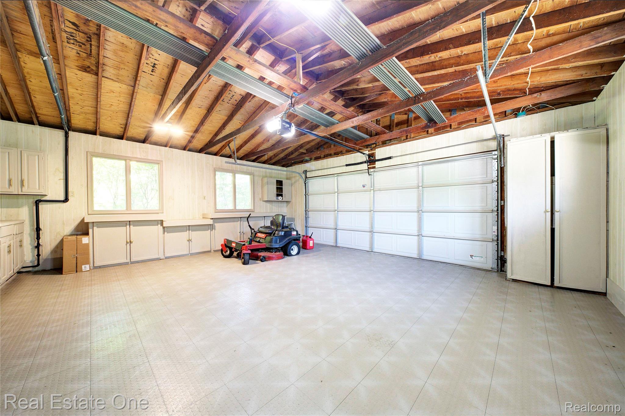 3125 West Commerce Road Milford, MI 48380 - Photo 49 of 63 Spacious garage featuring exposed wood ceiling beams, a double garage door, multiple windows, built-in cabinetry, and tile flooring