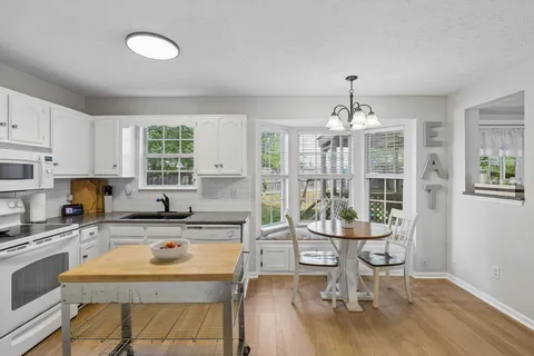 a kitchen with stainless steel appliances granite countertop a stove top oven a sink dishwasher a dining table and chairs with wooden floor