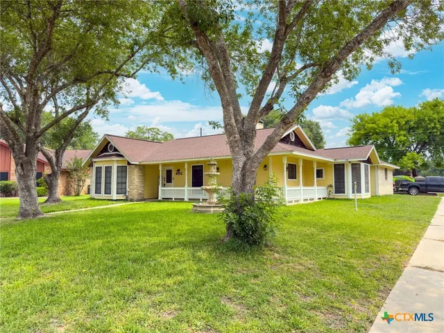 a tree in front of a brick house next to a yard