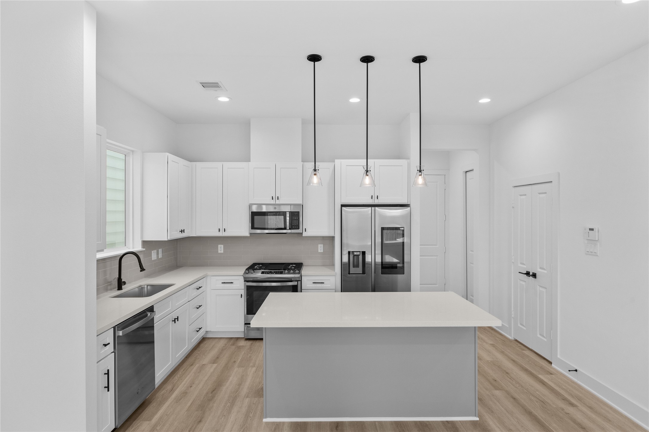 3426 Bolin Road Houston, TX 77092 - Photo 4 of 34 This is a modern, bright kitchen featuring white cabinetry, stainless steel appliances, and a center island with pendant lighting, set against light color flooring.