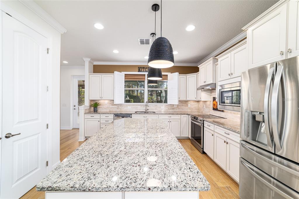 9710 Southwest 76th Lane Road Ocala, FL 34481 - Photo 15 of 45 a large kitchen with stainless steel appliances kitchen island granite countertop a refrigerator a stove a sink a dining table and chairs with wooden floor