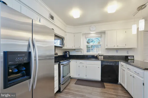 a kitchen with stainless steel appliances granite countertop a stove a refrigerator a kitchen island a dining table and chairs with wooden floor