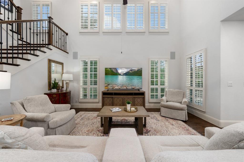 531 Sandy Lane Flower Mound, TX 75022 - Photo 15 of 32 Two-story living area featuring a grand staircase with dark wood treads and wrought iron balusters, expansive windows with plantation shutters and built-in ceiling speakers