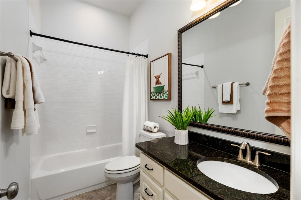 531 Sandy Lane Flower Mound, TX 75022 - Photo 9 of 32 Bathroom right outside front bedroom featuring a white subway tile shower surround, a bathtub, a dark stone vanity countertop, a large framed mirror, and a single vanity sink with a brushed nickel faucet