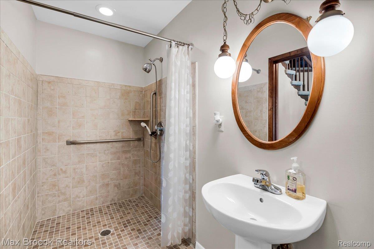 217 Stonetree Circle Rochester, MI 48309 - Photo 24 of 44 Bathroom featuring a pedestal sink, oval wood-framed mirror, and a tiled shower enclosure