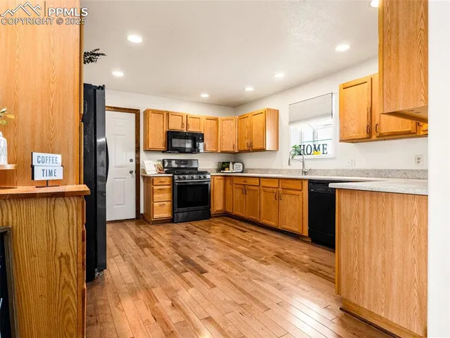 a kitchen with stainless steel appliances granite countertop wooden cabinets a sink a stove a refrigerator and island with wooden floor