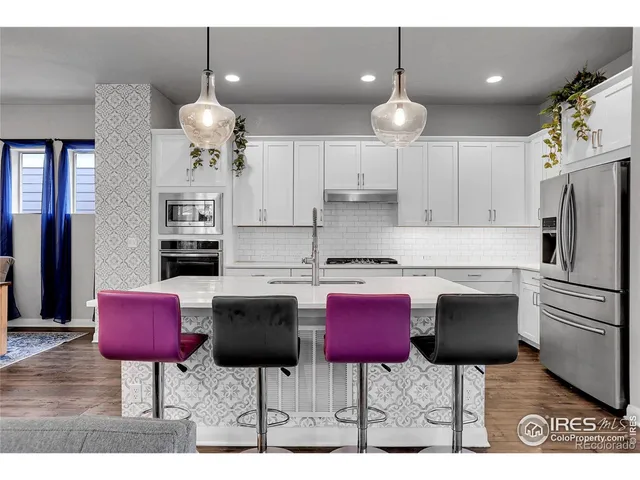 a kitchen with stainless steel appliances kitchen island granite countertop a dining table chairs and a refrigerator