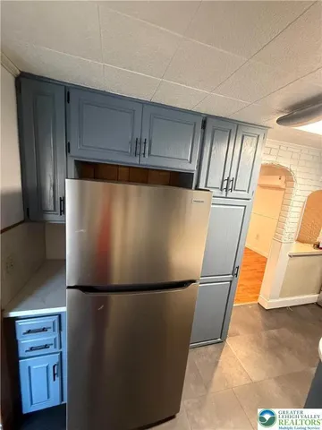 a view of a refrigerator in kitchen and an empty room with wooden floor