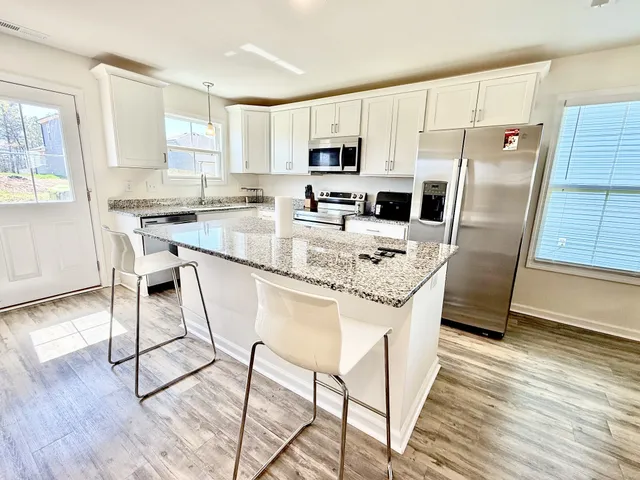 a kitchen with stainless steel appliances granite countertop a refrigerator a stove a sink and white cabinets with wooden floor