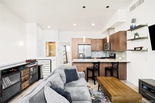 a living room with stainless steel appliances furniture a rug and a kitchen view