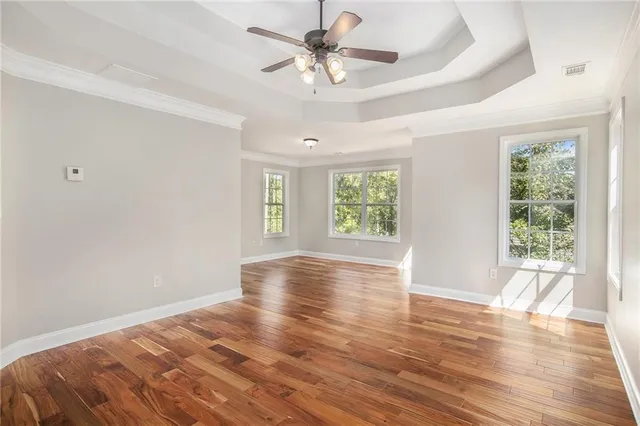 a view of an empty room with window a chandelier fan and wooden floor