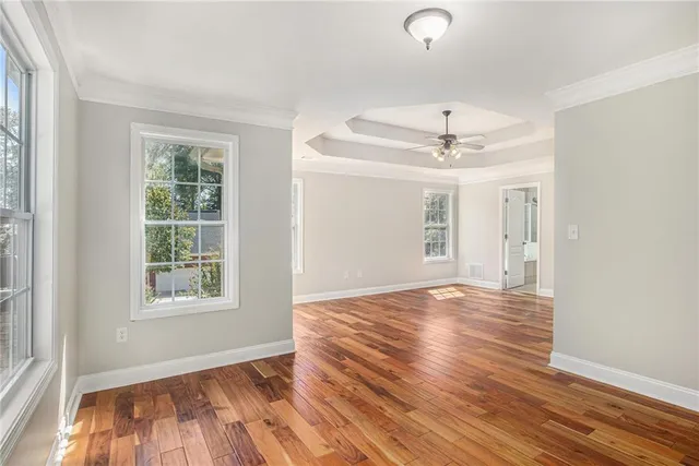 an empty room with wooden floor chandelier fan and windows