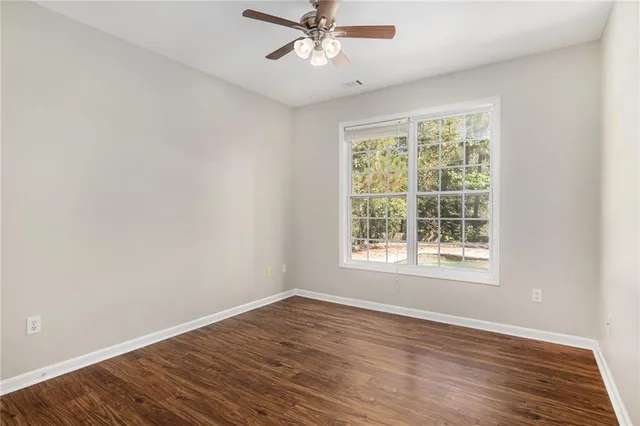 an empty room with wooden floor chandelier fan and windows