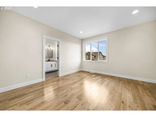a view of an empty room and a kitchen with wooden floor
