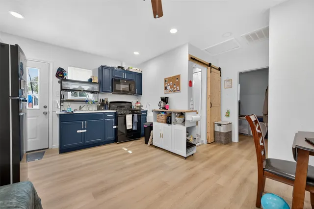 a kitchen with stainless steel appliances kitchen island granite countertop a refrigerator oven a sink a dining table and chairs with wooden floor