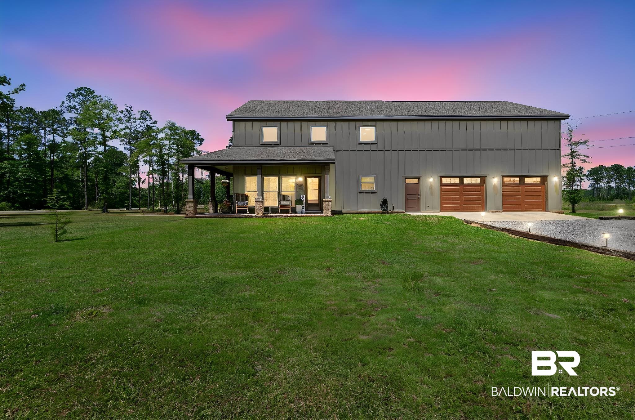 11025 Creax Road Axis, AL 36505 - Photo 3 of 45 Two-story structure with board-and-batten siding, a covered porch with stone-clad columns, a two-car garage with wood-finish doors, and a gravel driveway with integrated lighting