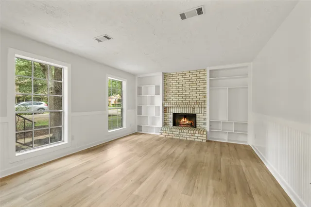 a view of an empty room with wooden floor fireplace and a window