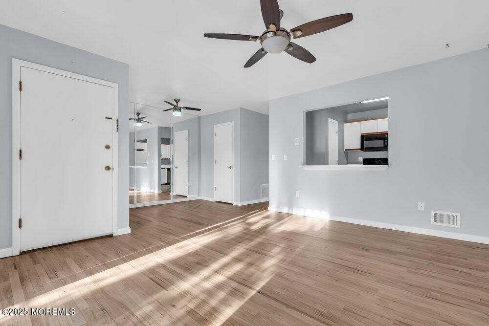 a view of an empty room with wooden floor and a ceiling fan
