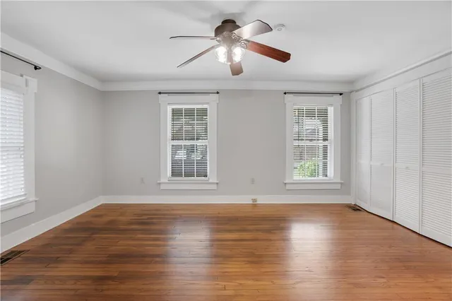 an empty room with wooden floor chandelier fan and windows