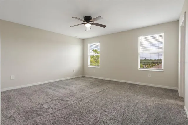 an empty room with ceiling fan and windows