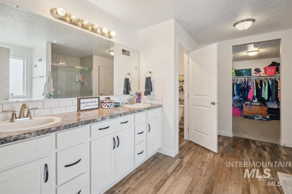 12656 Brun Street Caldwell, ID 83607 - Photo 14 of 39 Bathroom featuring a walk in closet, a textured ceiling, double vanity, a shower stall, and light wood-style flooring