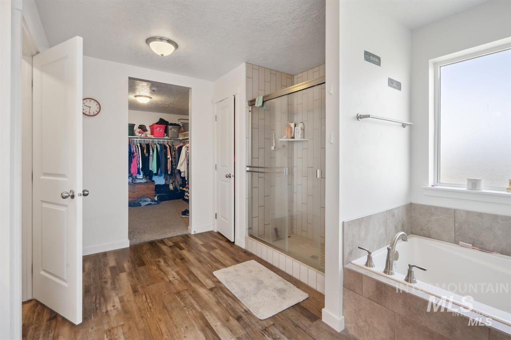 12656 Brun Street Caldwell, ID 83607 - Photo 15 of 39 Bathroom featuring a textured ceiling, a spacious closet, a bath, dark wood-style flooring, and a stall shower
