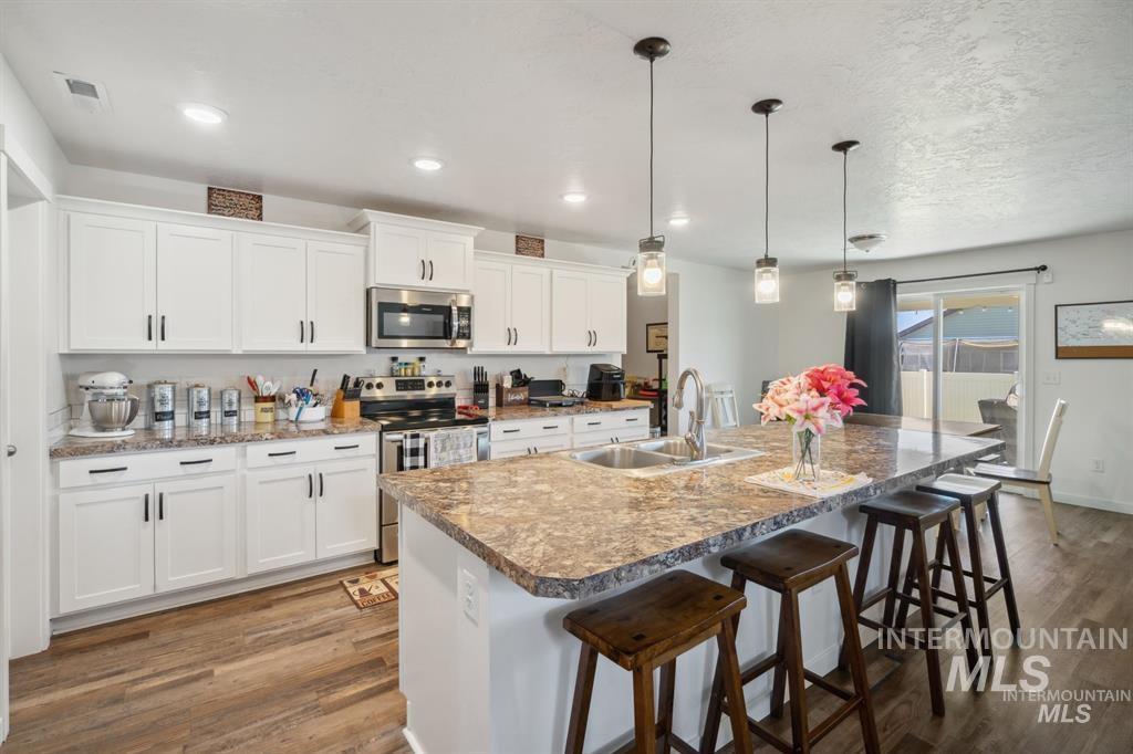 12656 Brun Street Caldwell, ID 83607 - Photo 6 of 39 Kitchen with stainless steel appliances, a breakfast bar area, white cabinets, and dark wood-style flooring