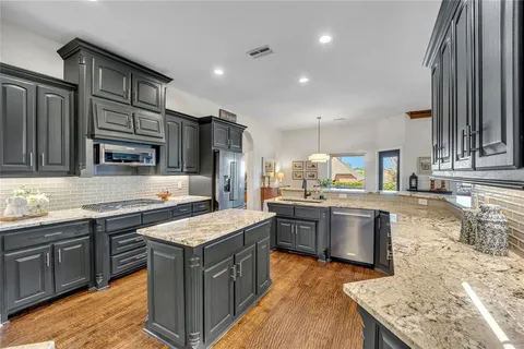 a kitchen with stainless steel appliances granite countertop a stove top oven a sink dishwasher and wooden cabinets with wooden floor