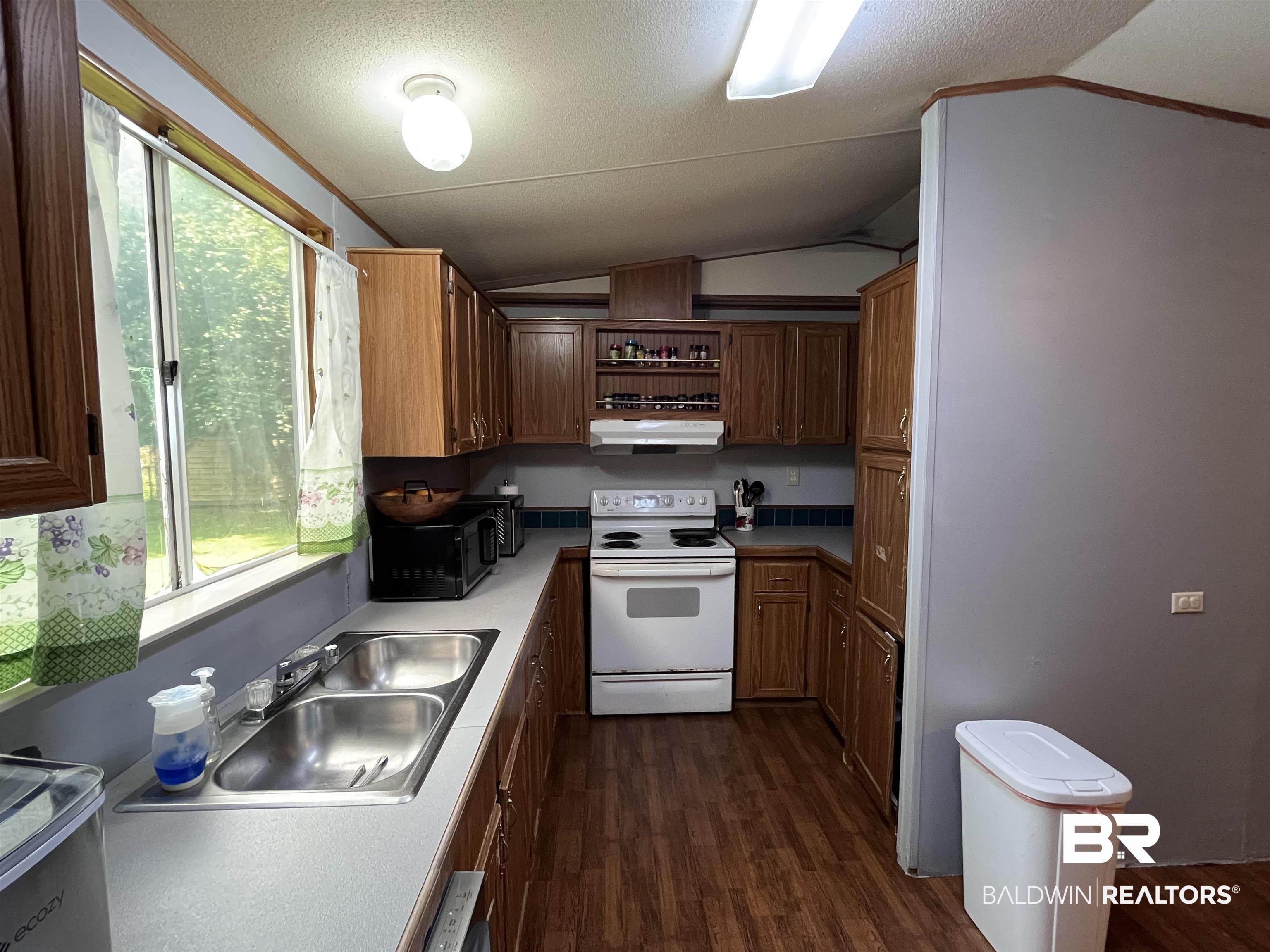 7719 Bermuda Drive Semmes, AL 36575 - Photo 5 of 10 Kitchen featuring electric stove, under cabinet range hood, vaulted ceiling, wood-style flooring, and healthy amount of natural light