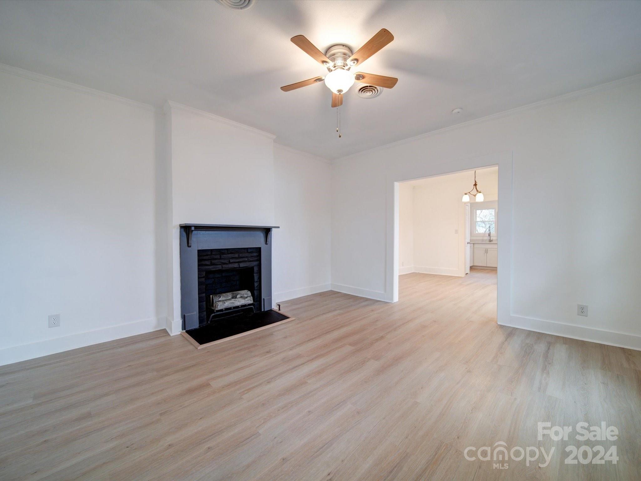 a view of an empty room with wooden floor a fireplace and a window
