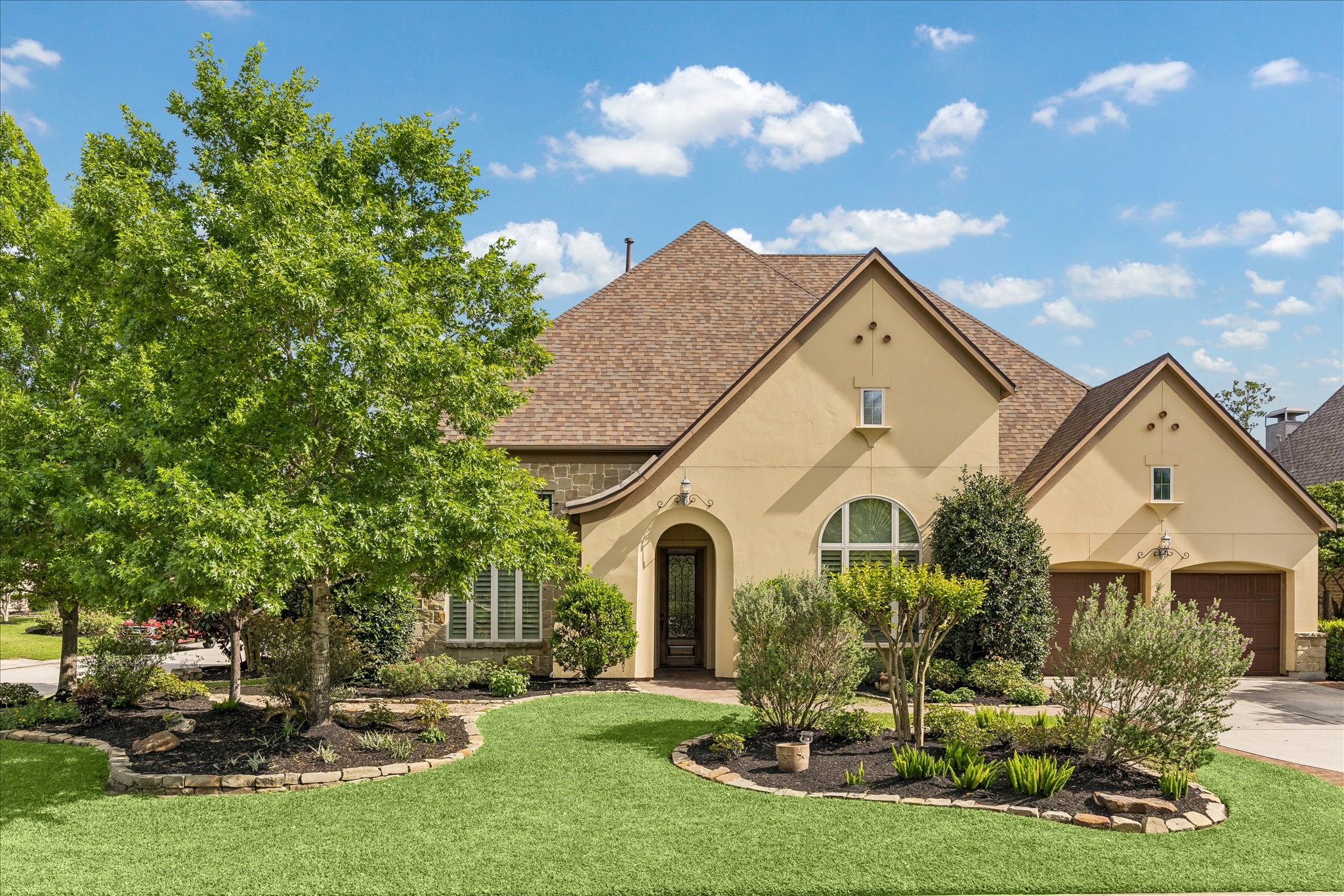 3 Tiburon Court Spring, TX 77389 - Photo 1 of 37 This is a charming two-story home featuring a warm beige exterior, a steeply pitched roof, and an inviting arched entryway. The front yard is beautifully landscaped with lush greenery and well-maintained garden beds, complemented by a spacious driveway.