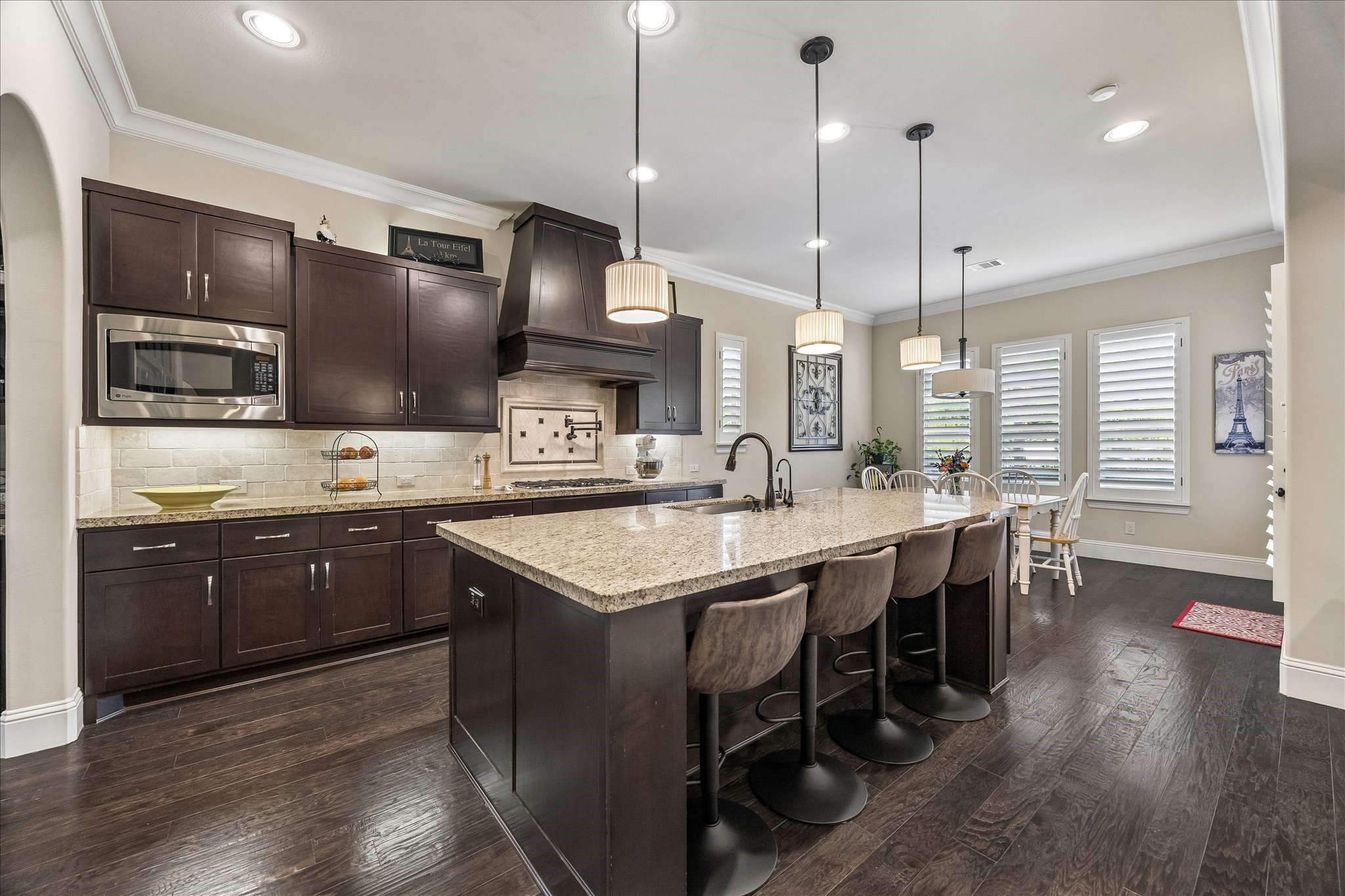 3 Tiburon Court Spring, TX 77389 - Photo 11 of 37 This spacious kitchen features dark wood cabinetry, granite countertops, and a large island with seating. It includes modern appliances, stylish pendant lighting, and an adjacent dining area with ample natural light from multiple windows.