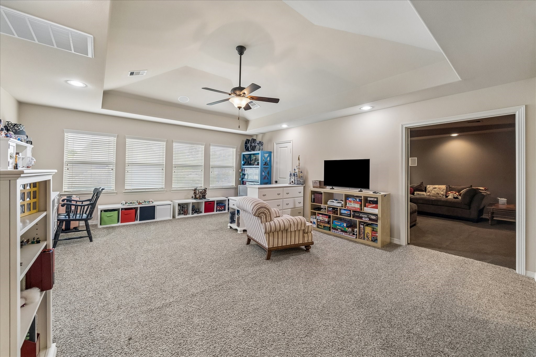 3 Tiburon Court Spring, TX 77389 - Photo 19 of 37 This spacious, carpeted family room features large windows for natural light, a ceiling fan, and ample storage. It's connected to a cozy entertainment area, making it ideal for relaxation and play.