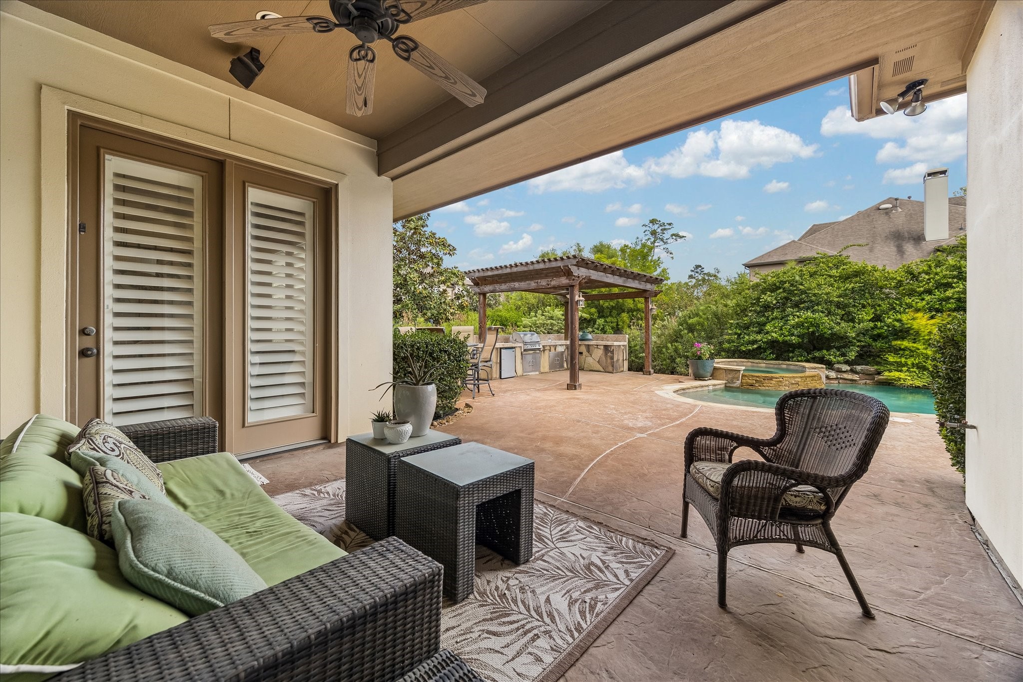 3 Tiburon Court Spring, TX 77389 - Photo 28 of 37 This inviting patio features cozy seating, a ceiling fan, and direct access to a beautifully landscaped backyard with a pool and pergola-covered outdoor kitchen, ideal for relaxation and entertaining.