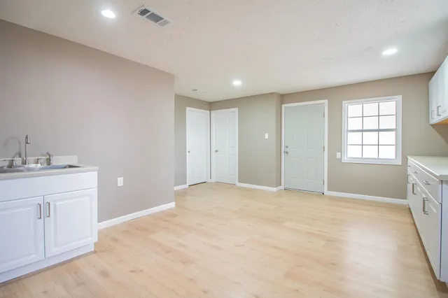 a view of an empty room with a window and a kitchen