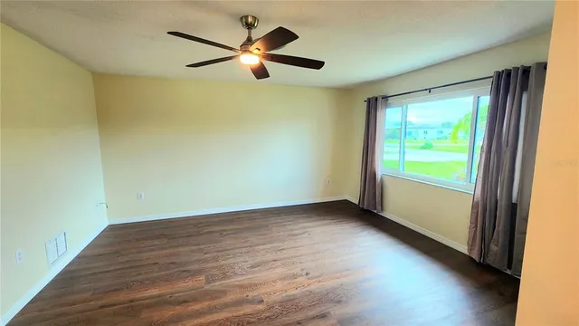 an empty room with wooden floor fan and windows