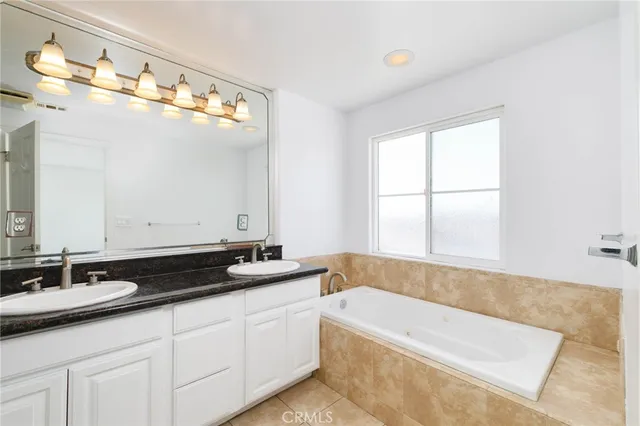 a bathroom with a granite countertop tub a double vanity sink and mirror