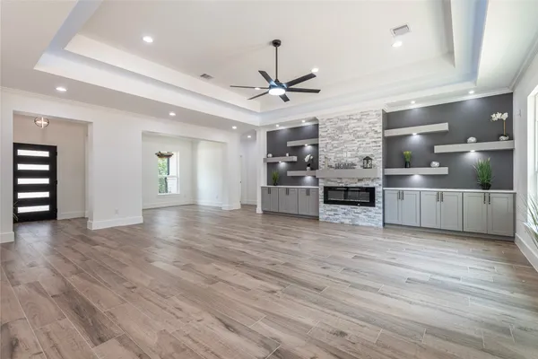 an empty room with wooden floor kitchen view and a ceiling fan