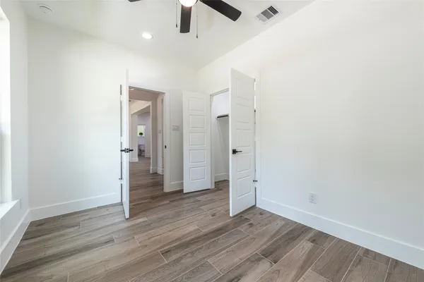 an empty room with wooden floor chandelier fan and windows