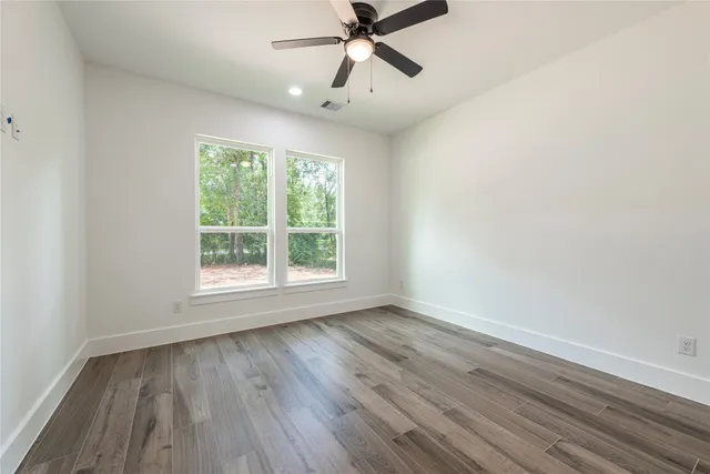 an empty room with wooden floor fan and windows