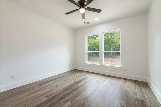 an empty room with wooden floor chandelier fan and windows