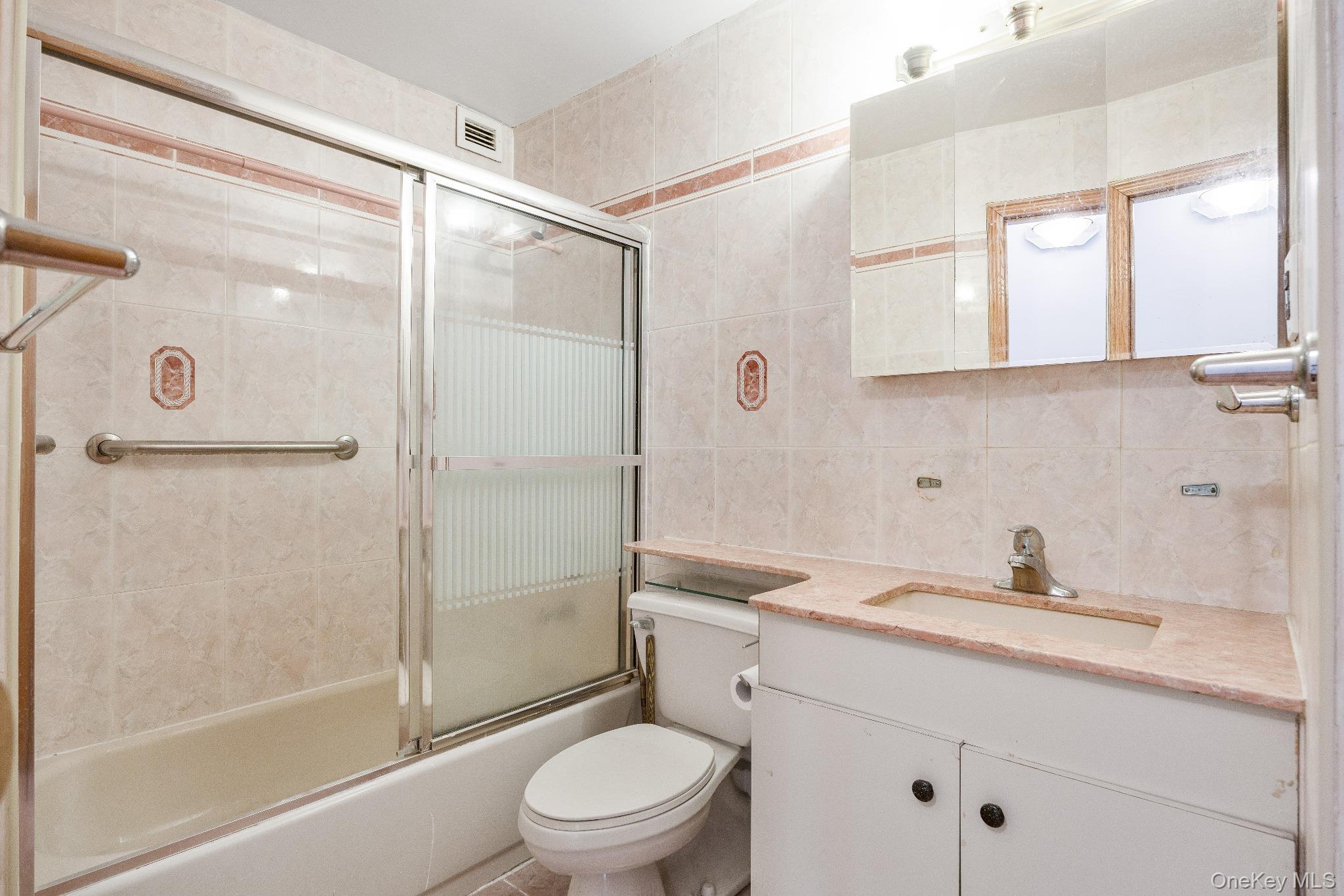 133-36 41st Road, Unit 8F Queens, NY 11355 - Photo 12 of 18 Bathroom – The full bathroom features tiled walls, a combination bathtub and shower with sliding glass doors, and a vanity with integrated sink and mirrored medicine cabinet for added storage. A clean, functional layout offers everyday convenience.