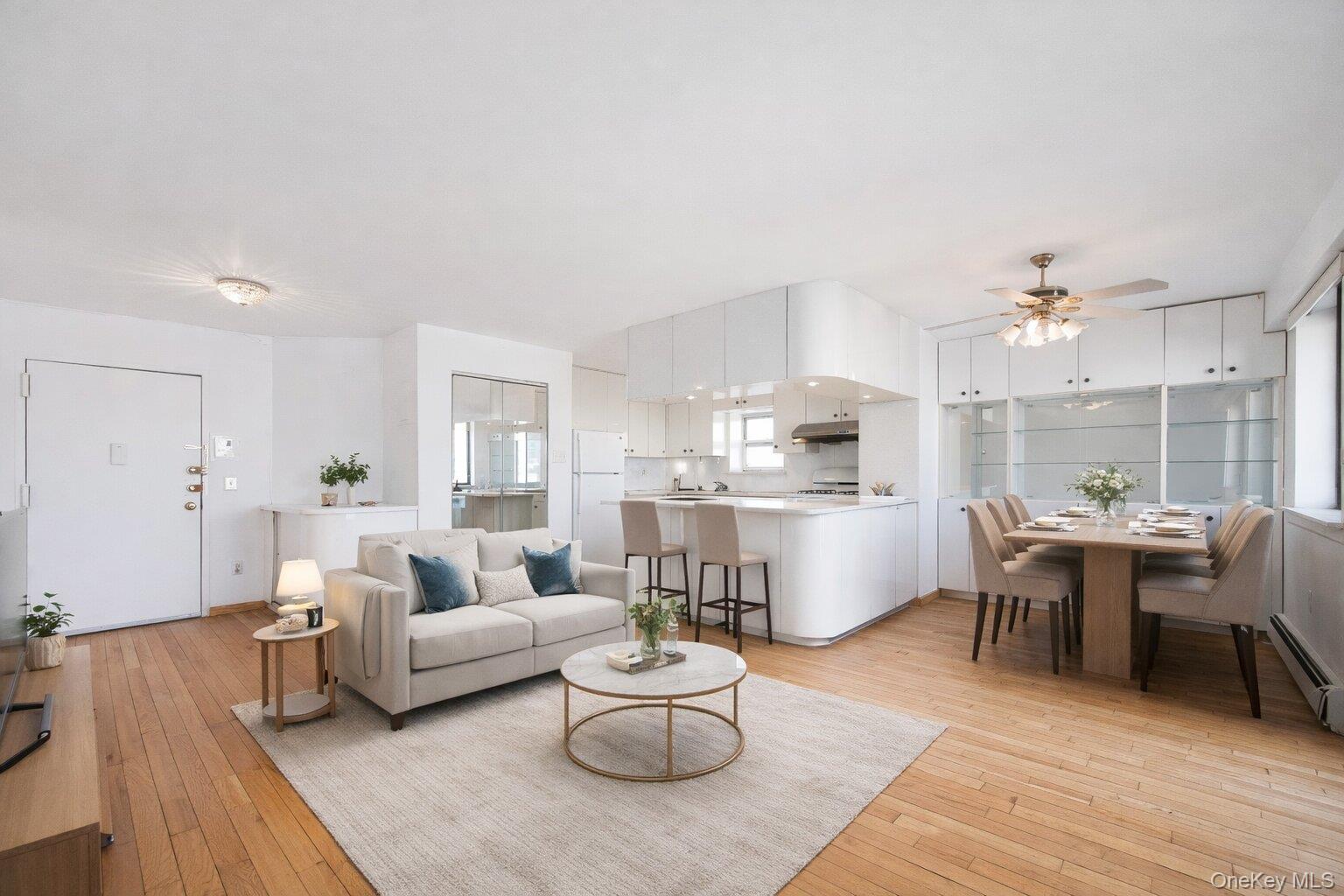 133-36 41st Road, Unit 8F Queens, NY 11355 - Photo 3 of 18 Living Room / Dining Area / Kitchen – This bright open-concept living and dining space features warm hardwood flooring and oversized windows that fill the home with natural light. The adjoining kitchen offers ample cabinetry, a convenient breakfast bar with seating, and a seamless layout ideal for everyday living and entertaining.