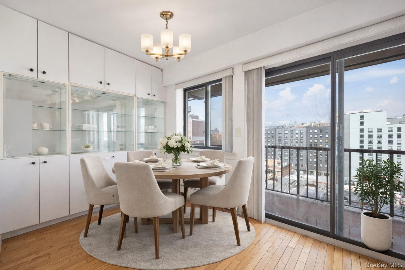 133-36 41st Road, Unit 8F Queens, NY 11355 - Photo 5 of 18 Dining Area / Balcony Access – The sunlit dining area features built-in cabinetry with glass display shelving and direct access to a private balcony through large sliding glass doors. Floor-to-ceiling windows showcase open city views while filling the space with natural light, creating a bright setting for everyday dining.