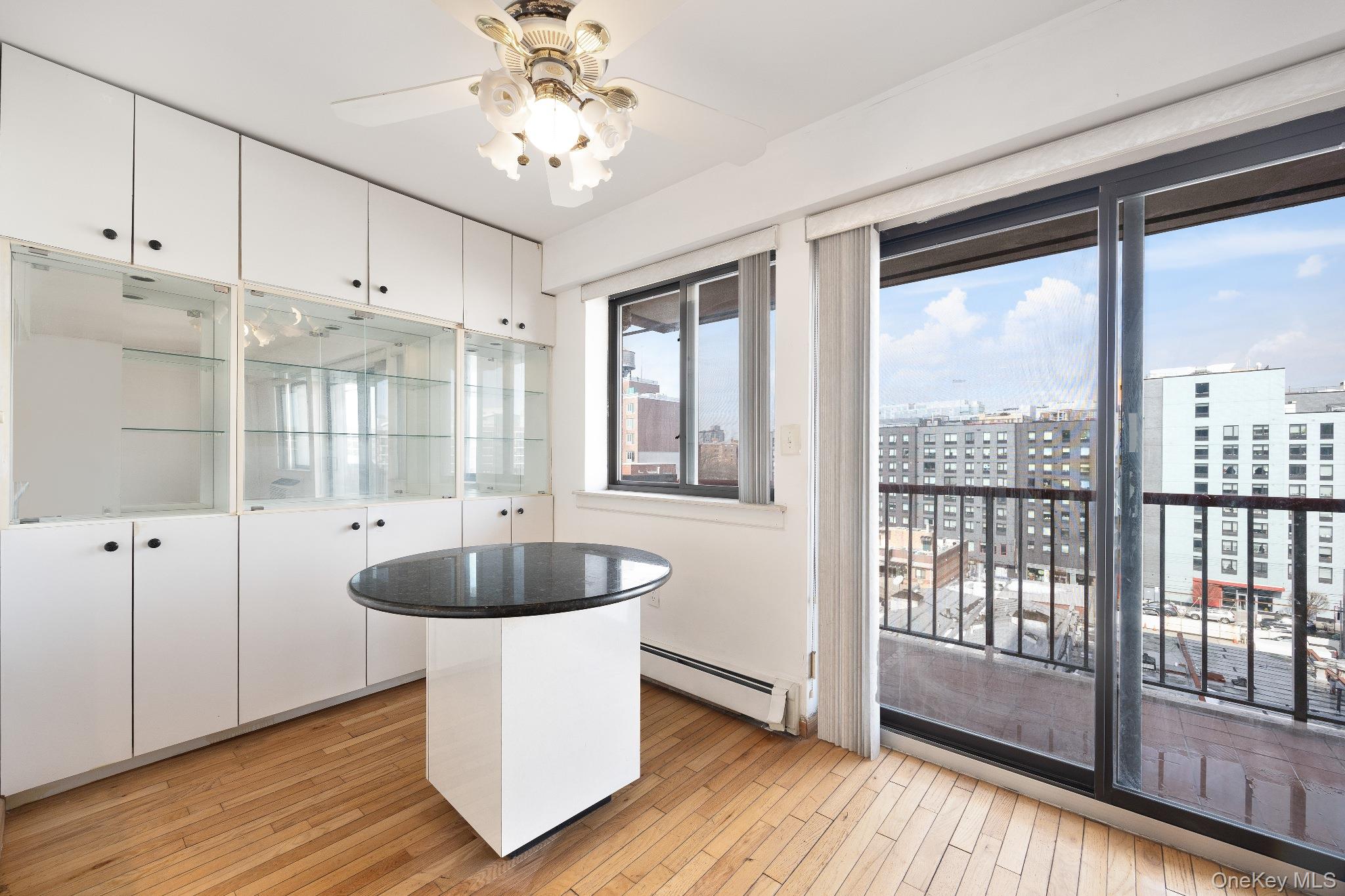 133-36 41st Road, Unit 8F Queens, NY 11355 - Photo 6 of 18 Dining Area / Balcony Access – The sunlit dining area features built-in cabinetry with glass display shelving and direct access to a private balcony through large sliding glass doors. Floor-to-ceiling windows showcase open city views while filling the space with natural light, creating a bright setting for everyday dining.