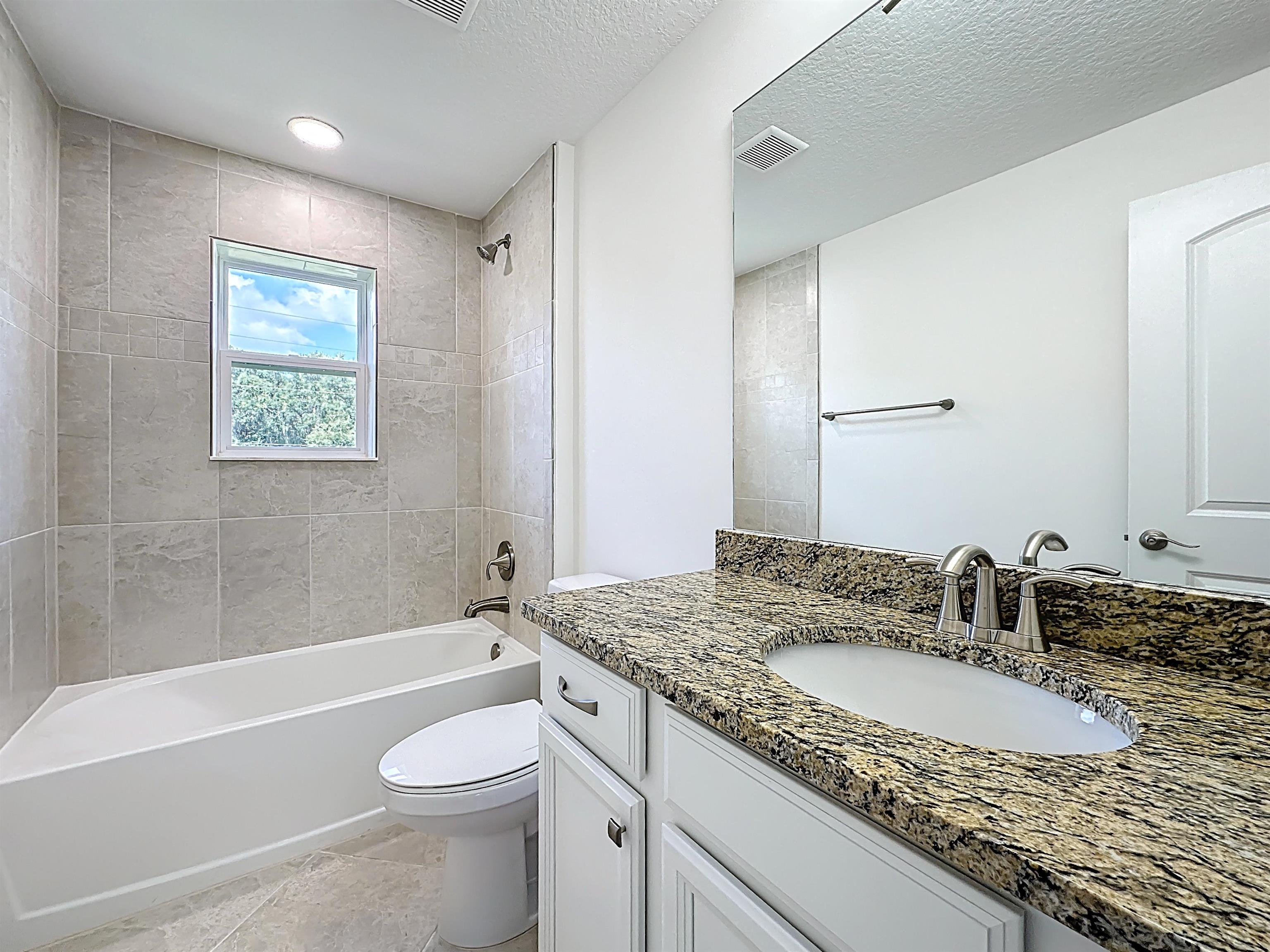 251 Grand Ravine Drive St. Augustine, FL 32086 - Photo 25 of 37 a bathroom with a granite countertop sink a toilet a mirror a bathtub and shower