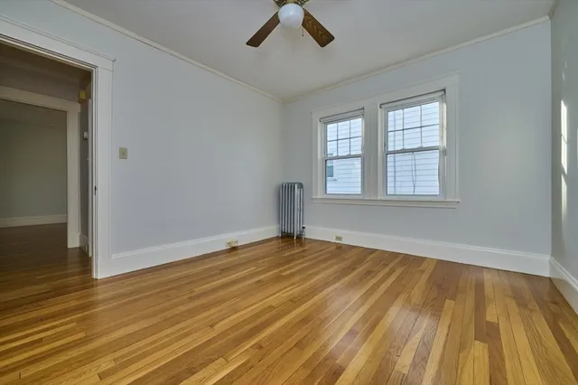 an empty room with wooden floor chandelier fan and windows
