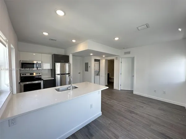 a large white kitchen with a large refrigerator a sink dishwasher with a stove and white cabinets with wooden floor