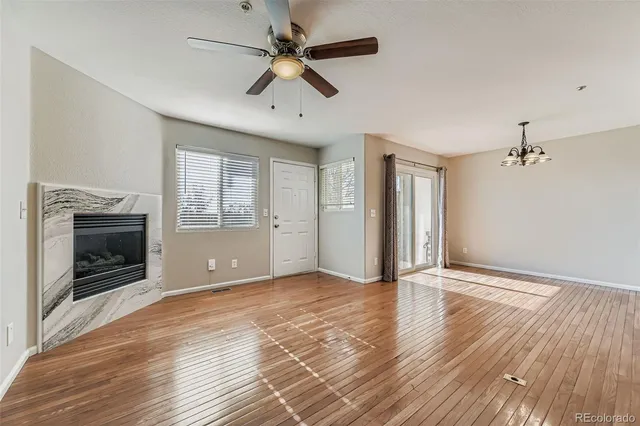 an empty room with wooden floor a ceiling fan a fireplace and windows